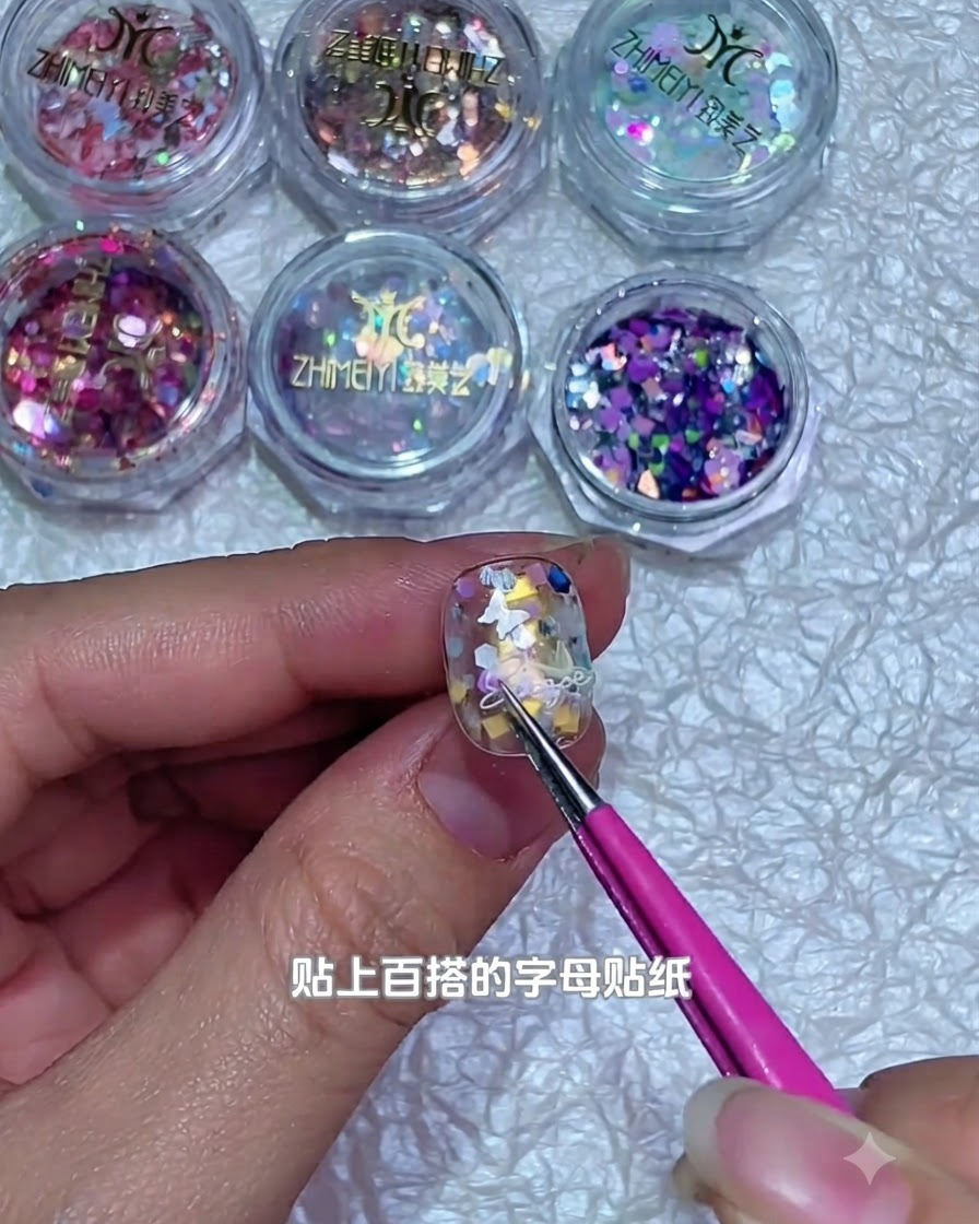 ピンセットを使用して、デコレーションされたジェルネイルの表面に小さな白い文字のステッカーを貼り付けている様子。