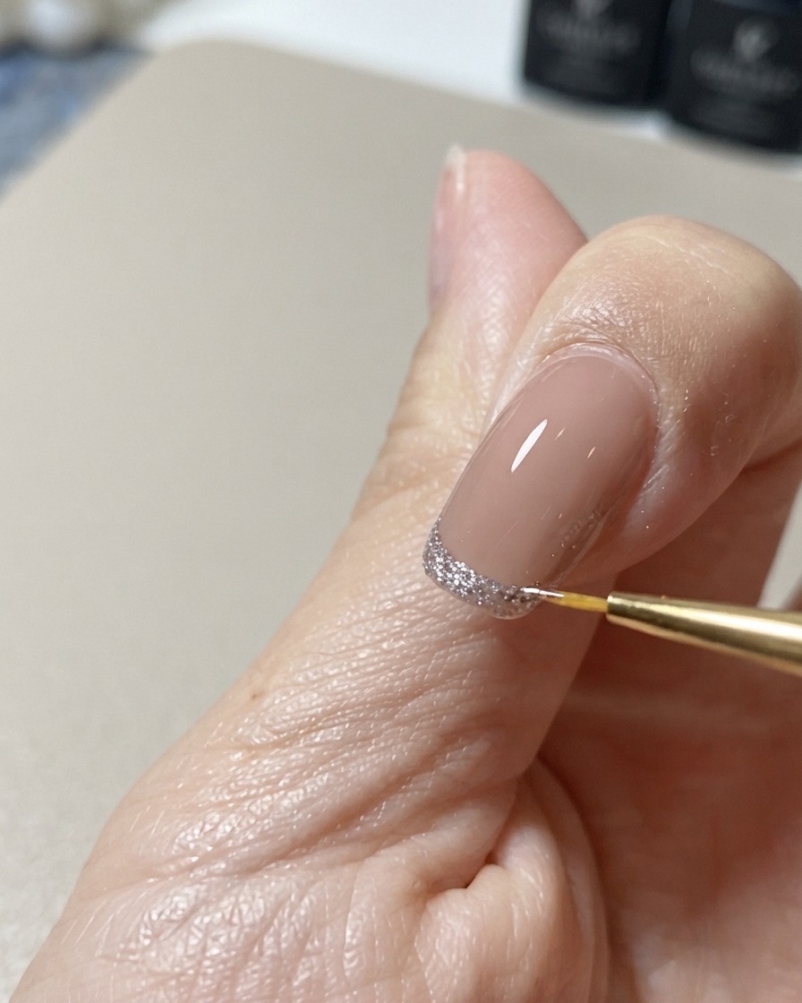 細いネイルアート用のライナーブラシを使って、きらめくキャッツアイの先端デザインの輪郭を整え、完璧に仕上げている様子。