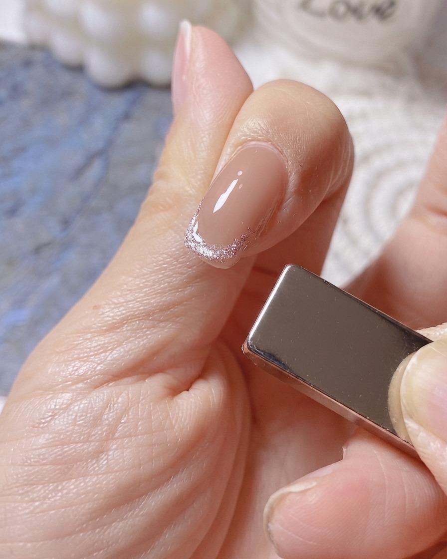 キャッツアイのフレンチネイルの先端に幅広の光るバンドを形成するため、指の右側にマグネットを配置している様子。