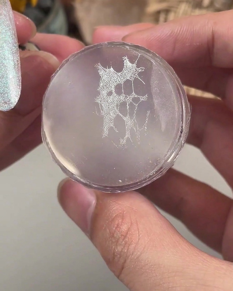 マニキュアを施したネイルに転写する準備ができた、繊細な白いレースパターンを持つクリアシリコンスタンパー。