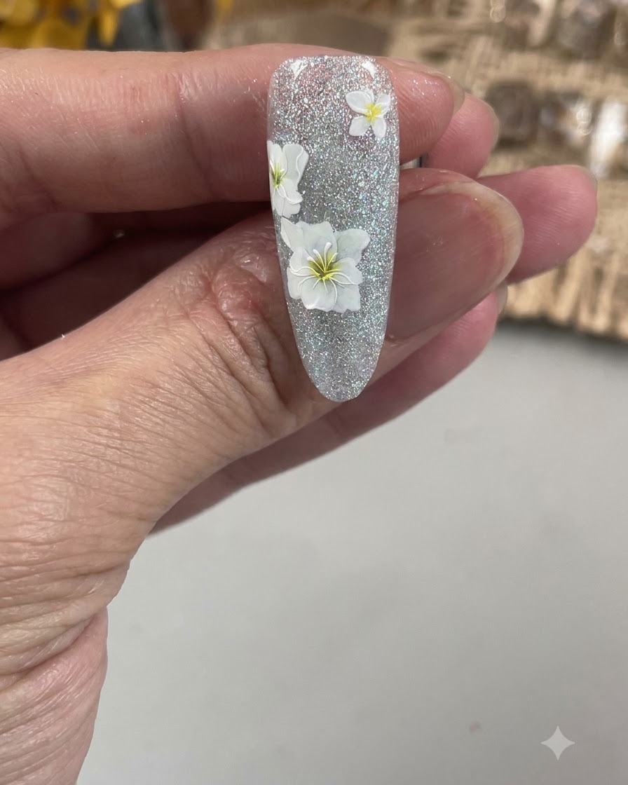 テクスチャーのあるネイル上の白い花の繊細な花びらの輪郭を、極細のネイルアートブラシで描いているクローズアップビュー。