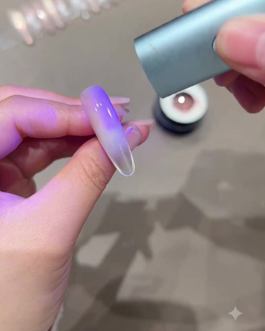 パープルグラデーションのキャッツアイ効果が現れた長めのネイルに、ミニUV LED硬化ライトをかざしている手。