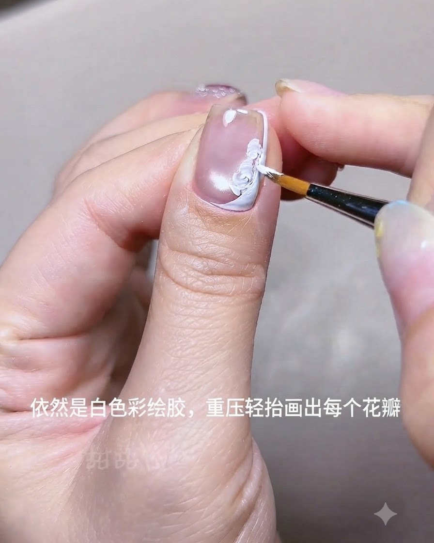 白いフレンチラインの近くで、細いライナーブラシを使って爪にアクリルジェルで白い花のペタルを描いているクローズアップ。