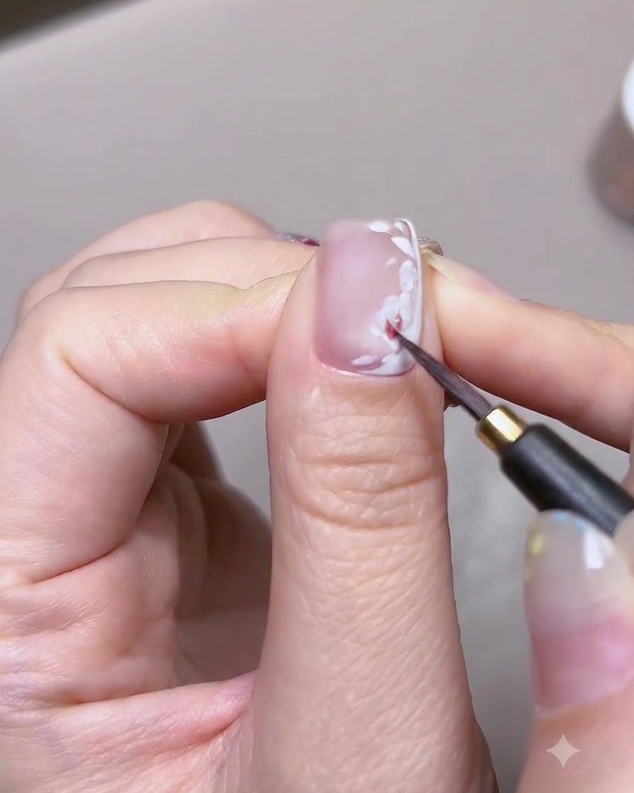 細いブラシを使って、ネイルアートのバラの白い花びらのベースに赤い水彩絵の具を塗っている詳細なクローズアップ。