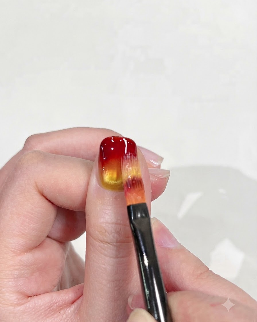 グラデーション効果を洗練するために、赤い先端をイエローベースに向けて下方に慎重にブレンドしているフラットネイルブラシ。