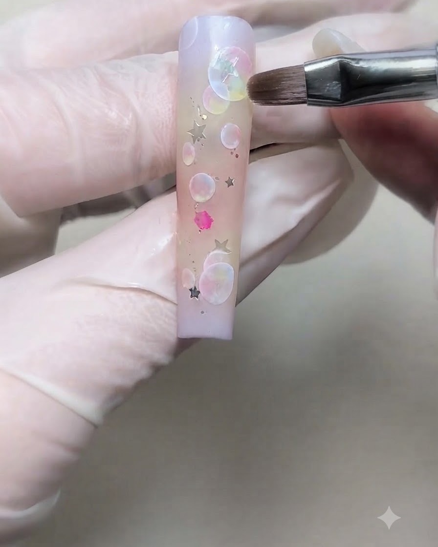 手袋を着用した手が、細いブラシを使ってグラデーションネイルの上にシルバースターグリッターを配置している様子。