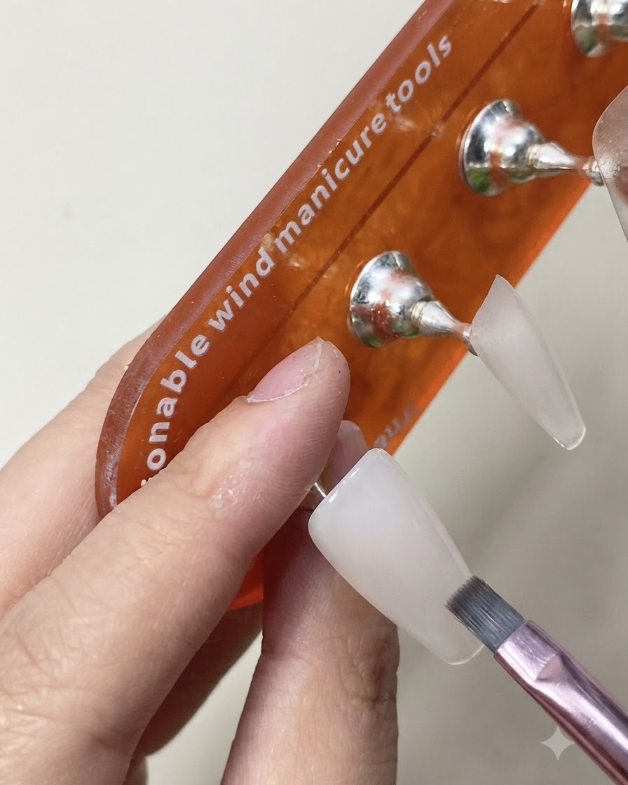 硬化させたミルキーホワイトのネイルエクステンションの上に、光沢のあるトップコートのレイヤーをブラシで塗布している様子。