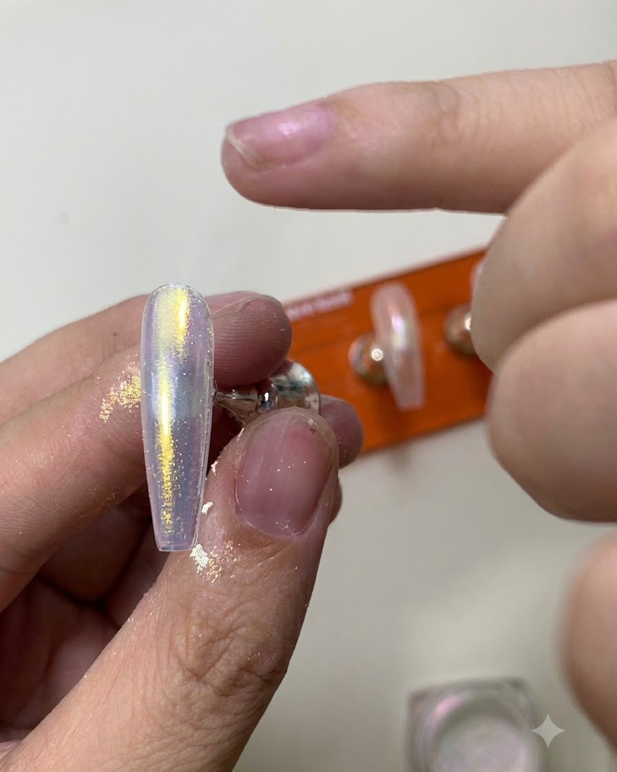 シリコン製のアプリケーターツールを使って、光沢のあるネイル表面にきらめくオーロラクロームパウダーを擦り込んでいる様子。