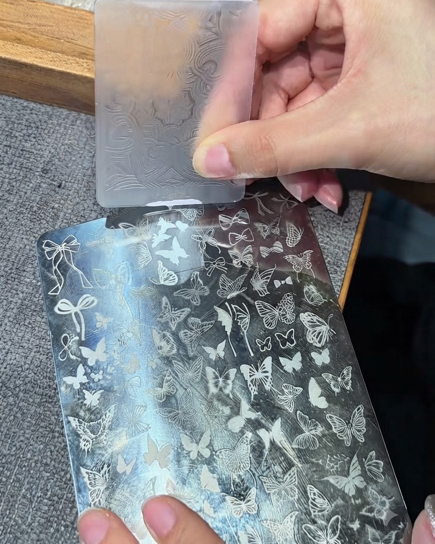 透明なシリコンスタンプヘッドが金属製スタンピングプレートに押し付けられ、白いデザインを拾い上げている様子。