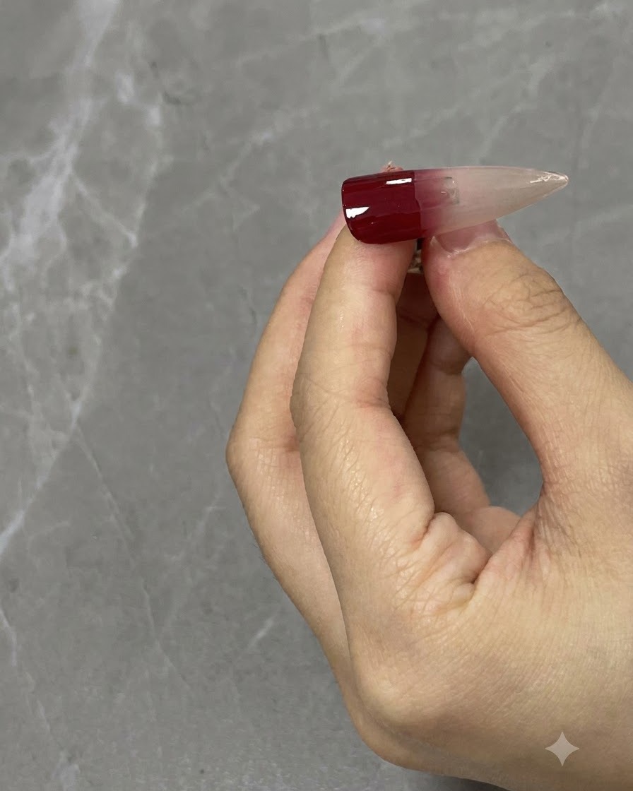 Eine Nahaufnahme eines Nagelpinsels, der einen weinroten Farbverlauf auf einer neutralen Nagelspitze nach unten hin verblendet.