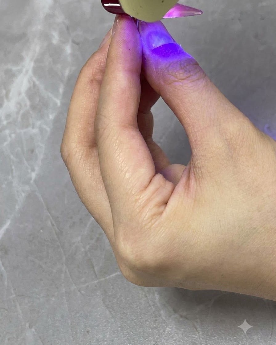 Eine tragbare UV/LED-Lampe härtet eine transluzente rote Verlaufsschicht auf einem fertigen Nagel aus.