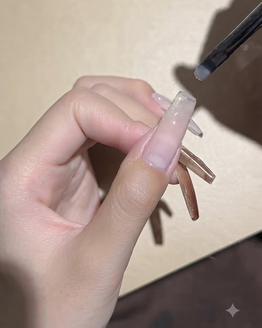 小さなジェルブラシが、整えられたネイルプレートの上に滑らかなクリアベースジェルのコートを塗布している様子。
