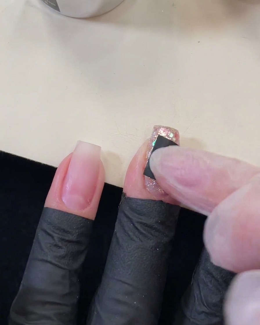 きらめくスパンコールネイルの上に、星型の切り抜きがある小さな黒いスクエアステッカーを指でしっかりと押さえている様子。