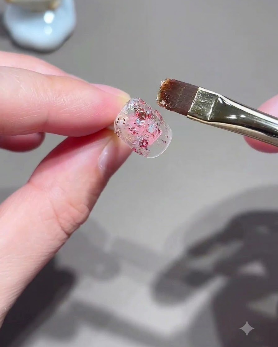 フラットなネイルブラシを使って、ネイルチップにピンクのグリッタージェルを塗っている様子。