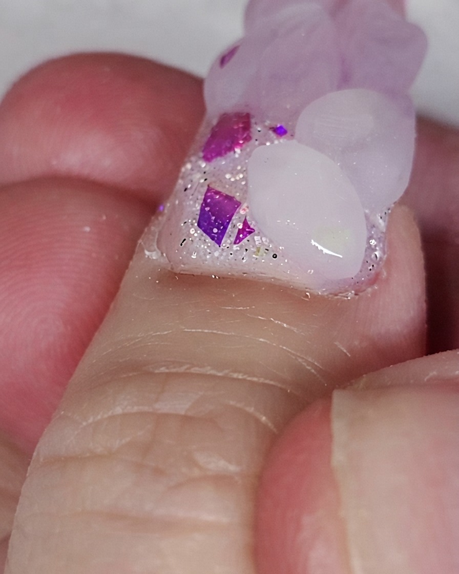 ハートの形を形成するために、グリッターネイルベースの上にピンクのアクリルビードを置いているネイルブラシ。