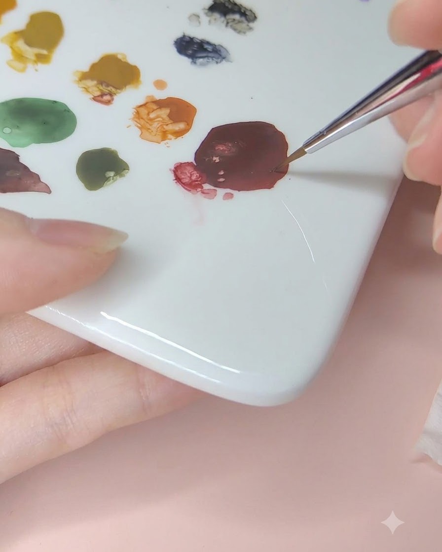 水を含ませた極細筆でセラミックパレット上の濃い赤色の水彩絵の具を溶かしている様子。