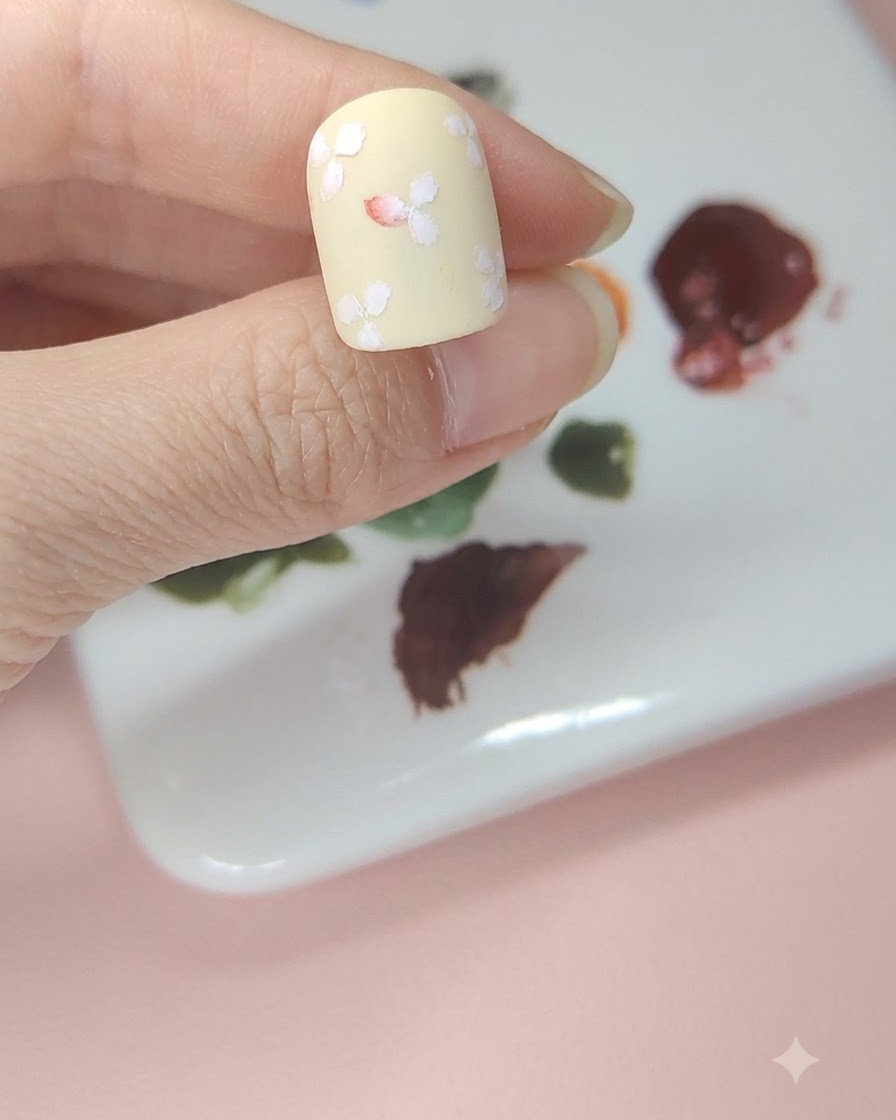 中央の白いお花の中心部分に赤い水彩絵の具をチョンとのせてふんわりと色づけたネイル。