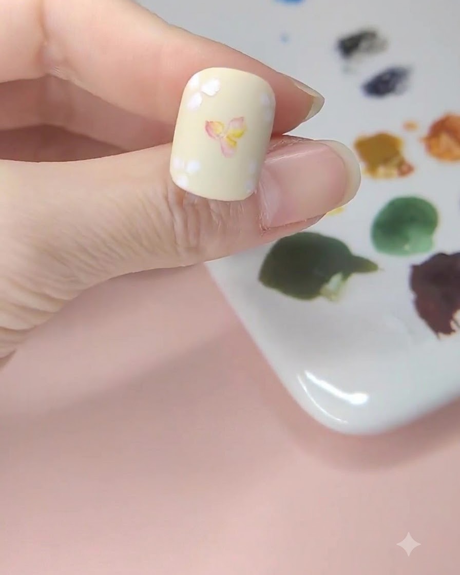お花と背景の余白部分に薄い黄色の水彩絵の具をふんわりとのせているネイル。
