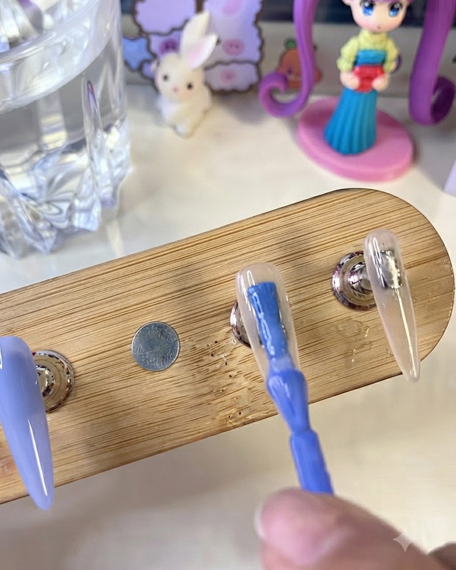 木製スタンド上のネイルチップに鮮やかなブルーのジェルポリッシュをブラシで塗っている様子。隣にはミルキーホワイトのベースが塗られたネイルがある。