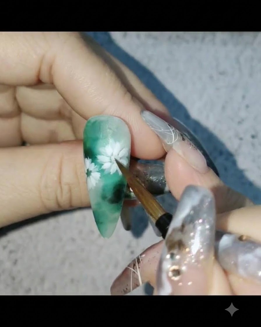 グリーンを基調としたフラワーネイルデザインの上から、ネイルブラシでマットトップコートを塗布している様子。