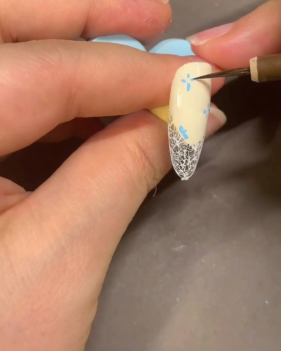 水彩筆を使い、ネイル上の青いマーカーの花びらをアルコールでぼかしてスモーキーな仕上がりにしている様子。