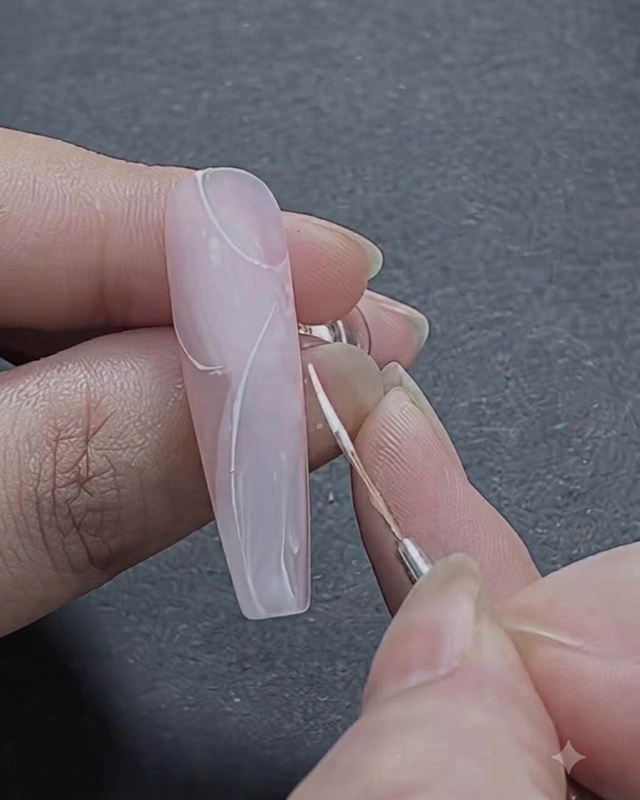 細いブラシを使用して、爪の上部にバラのパターンの最初の湾曲した白いストロークのアウトラインを描いている様子。