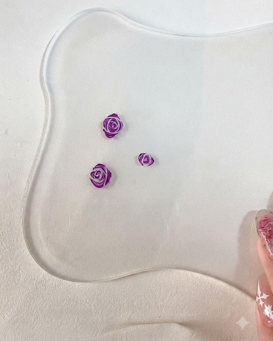 彫刻された3Dローズの花びらのエッジに、細いネイルアートブラシで詳細な濃い紫色の輪郭を追加しているクローズアップ画像。