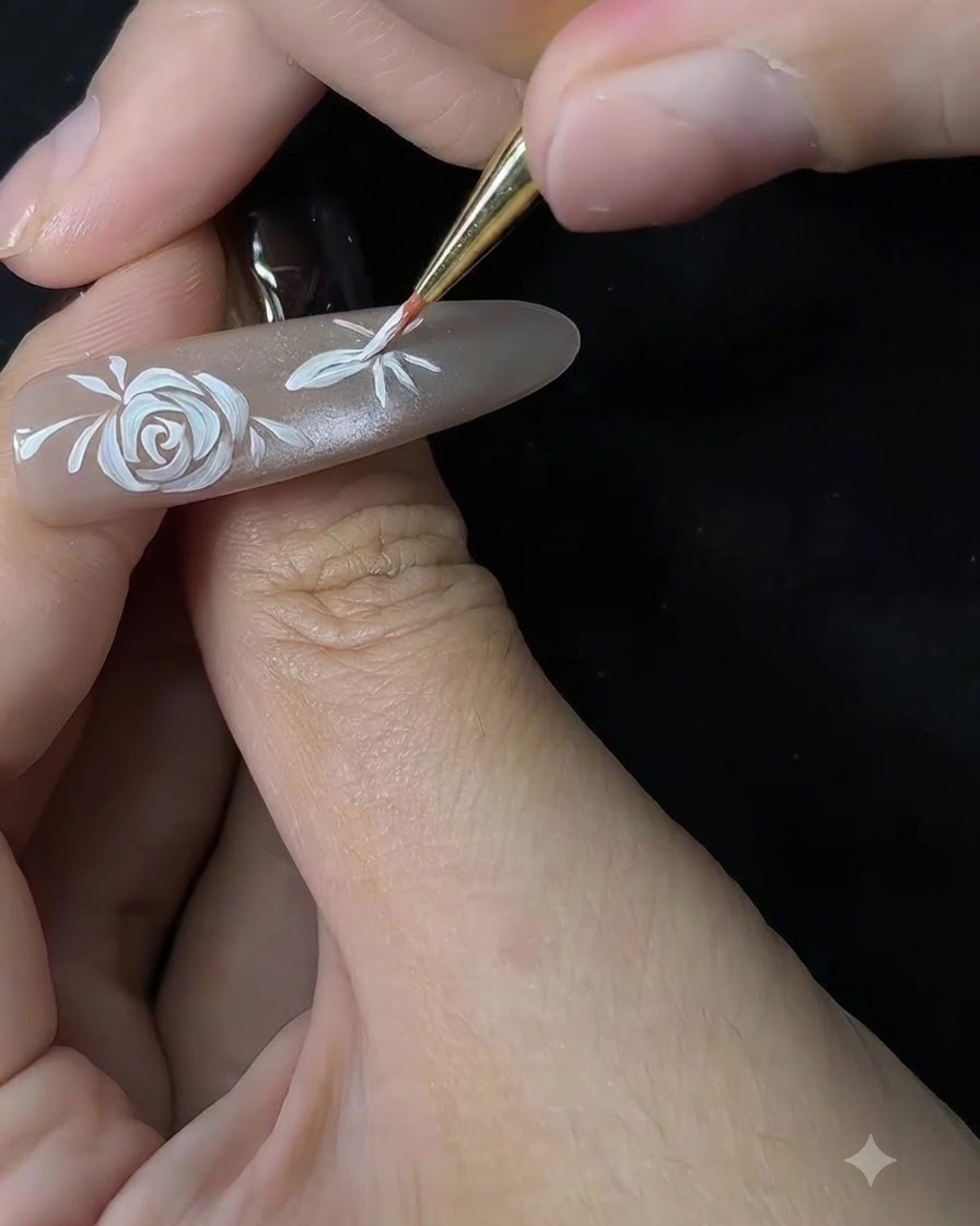 ヌードカラーのネイルチップ上で、極細のブラシが2つ目の花びらの形を描き始めている様子を捉えたクローズアップ写真。