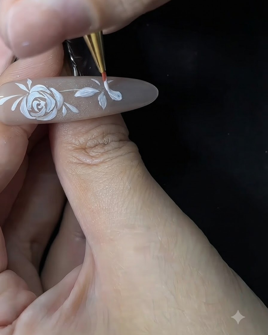 ジェルネイルチップ上で、ネイリストが極細のブラシを使って小さな花の白い花びらを整え、太さを調整している様子。