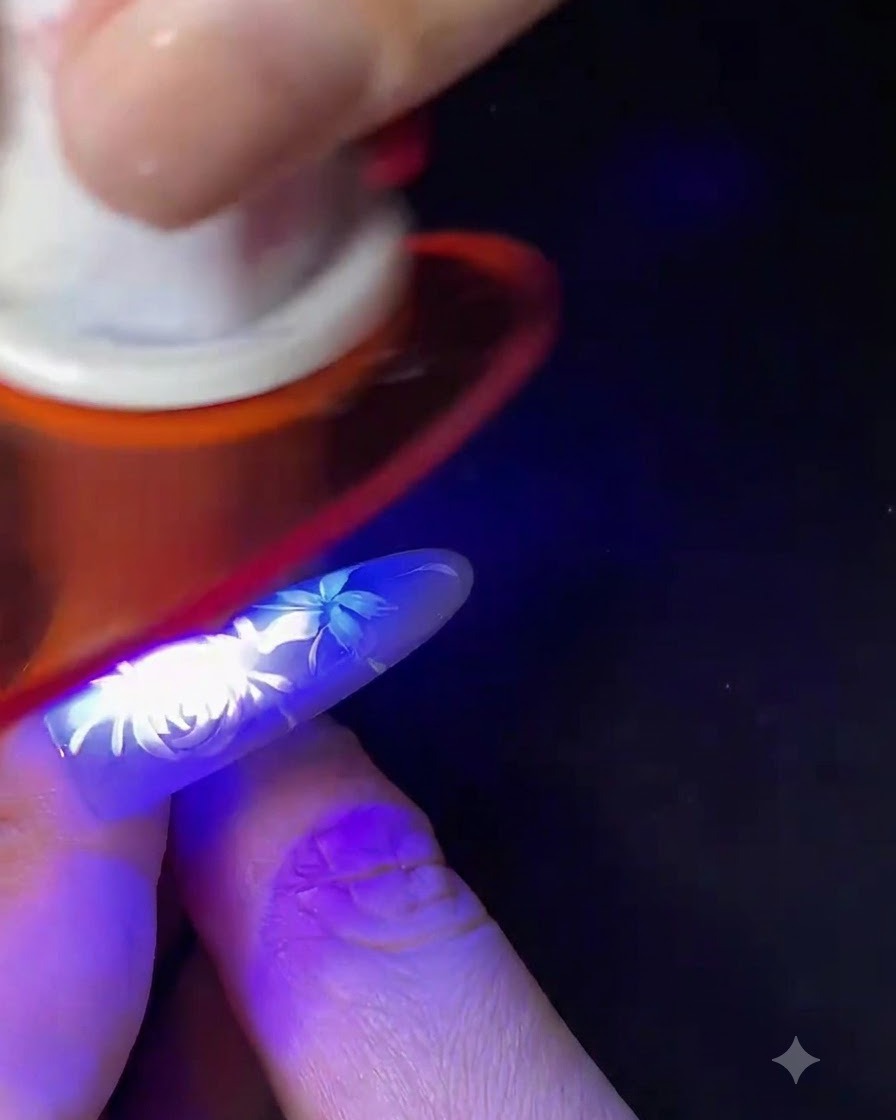 完成した白いフラワーネイルアートを施した指が、小型の青いUV/LEDネイルランプの下で硬化している様子。