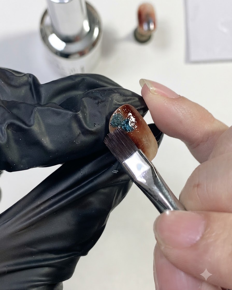 硬化済みのアンバーネイルの脇に、きらめくブルーのマグネットキャッツアイジェルを小さなドット状に置いている様子。