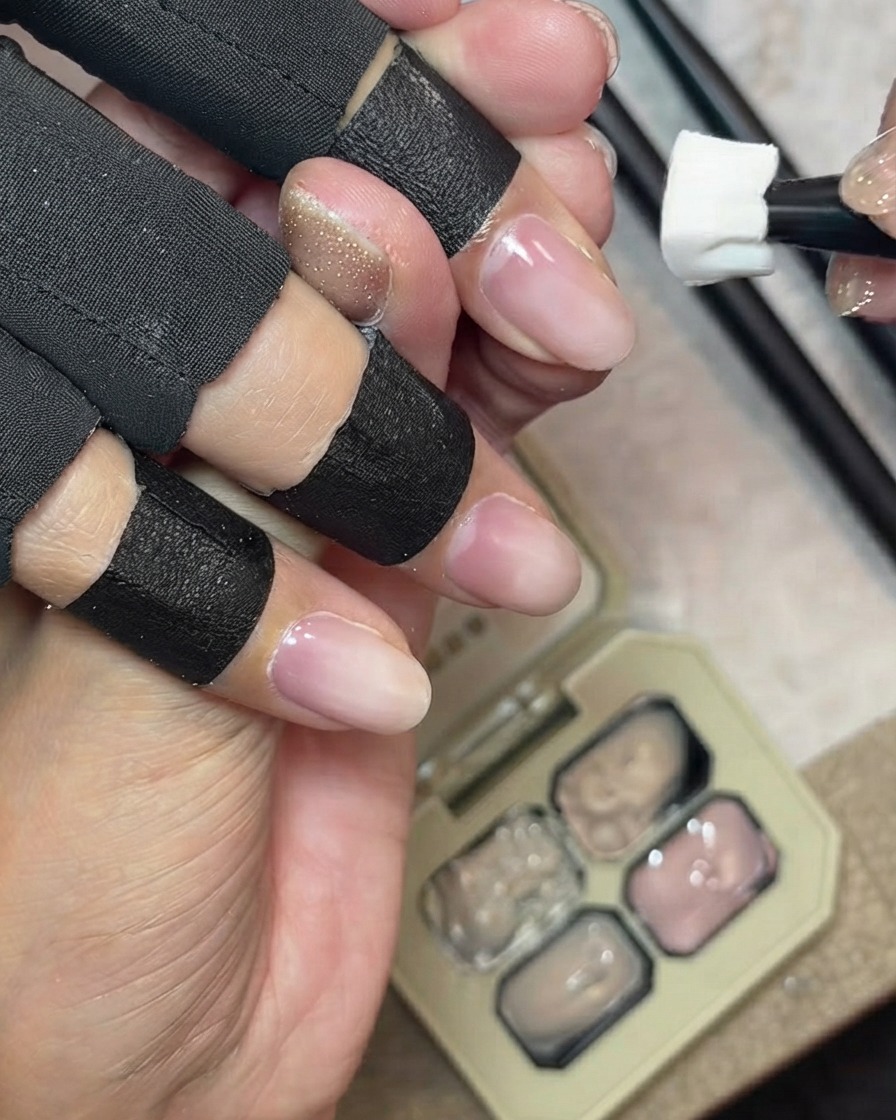 背景にジェルパレットを置きながら、スポンジツールが自爪のフリーエッジにミルキーヌードカバージェルをポンポンと叩き込んでいる様子。