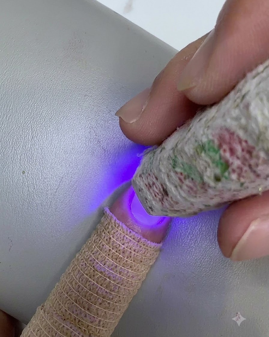 模様入りのミニUV/LEDライトを爪の先端にかざし、ブレンドしたクリアジェルの層を硬化させている様子。