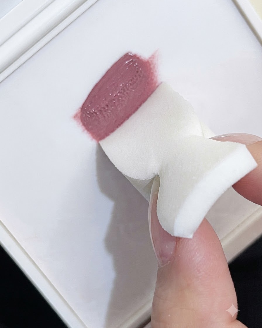 白いフォームスポンジのエッジで、パレットからモーブカラーのパッティングジェルを取り込んでいる様子。