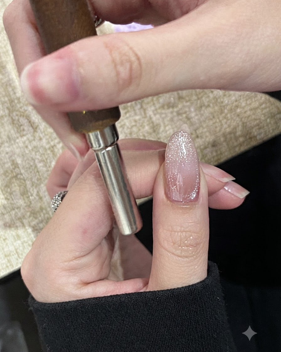 硬化前のキラキラしたキャッツアイジェルネイルの先端に沿って、円筒形のマグネットを水平に持っている手。