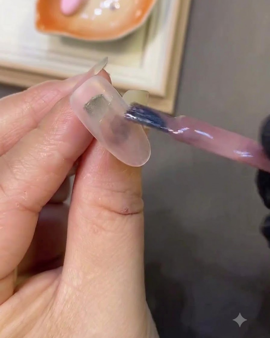 ミルキーホワイトのネイルの上に、ブラシでライトピンクのキャッツアイジェルを塗っている様子。