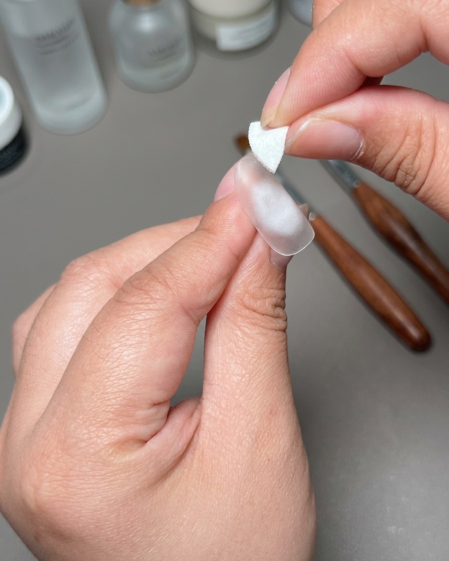 準備されたネイルチップの中央に小さな白い粘着パッチを当てている手