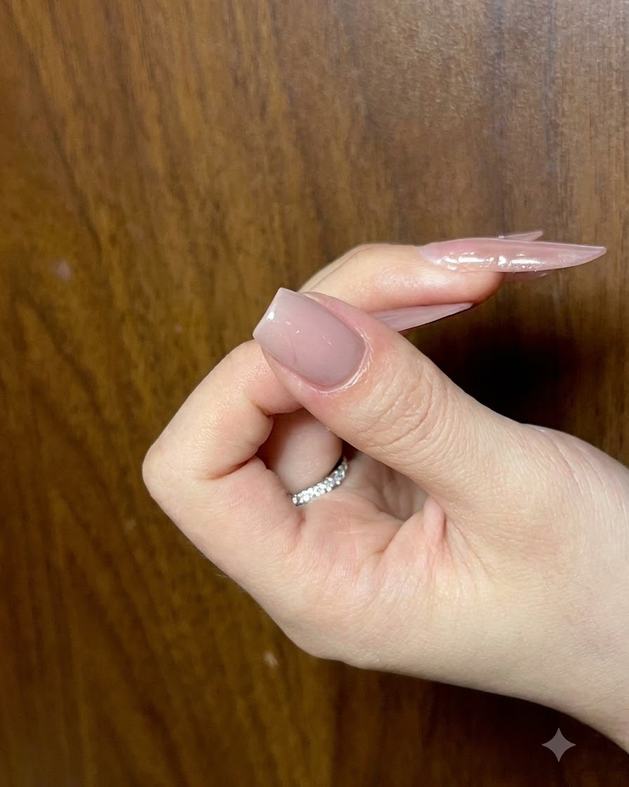 滑らかさを確認するために角度を変えて見られた、完成したヌードベースレイヤーを持つネイルを保持している手。