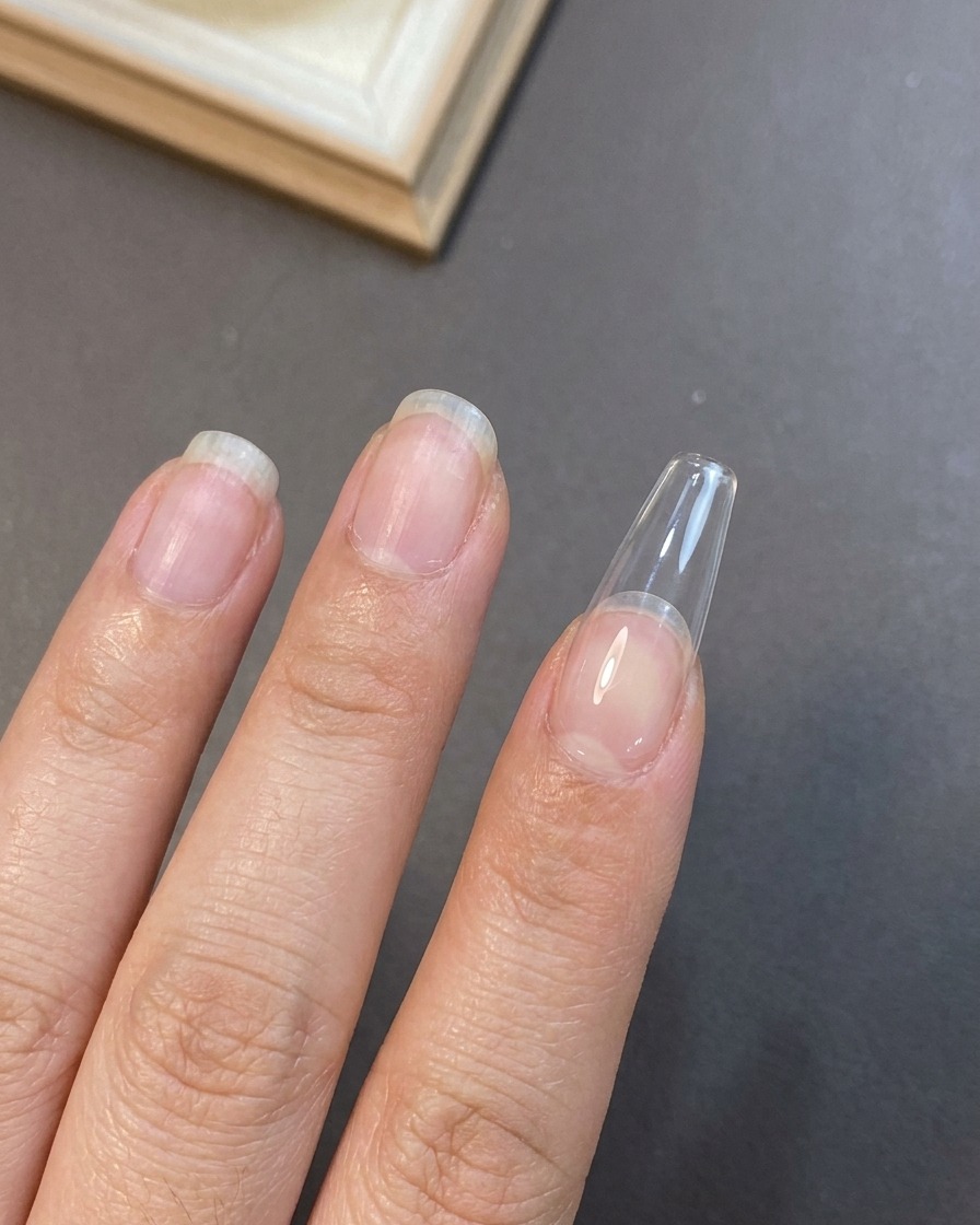 長さ出しをした爪や自爪の表面に、ジェルブラシを使って1層目のヌードカラーのベースを薄く塗布しているクローズアップビュー。