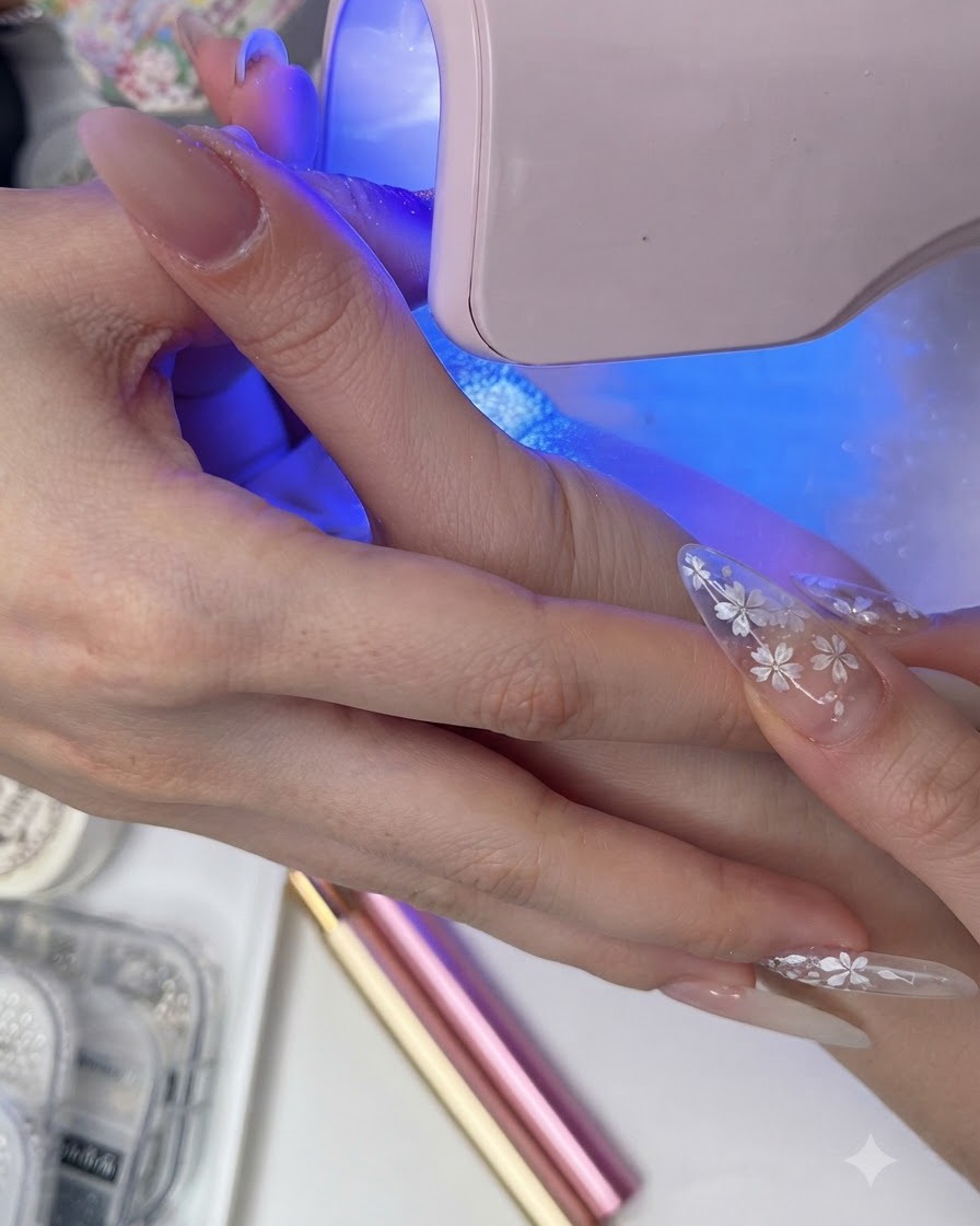 ピンクのUV/LEDランプの下で、ネイル表面にトップコートを硬化させている手。