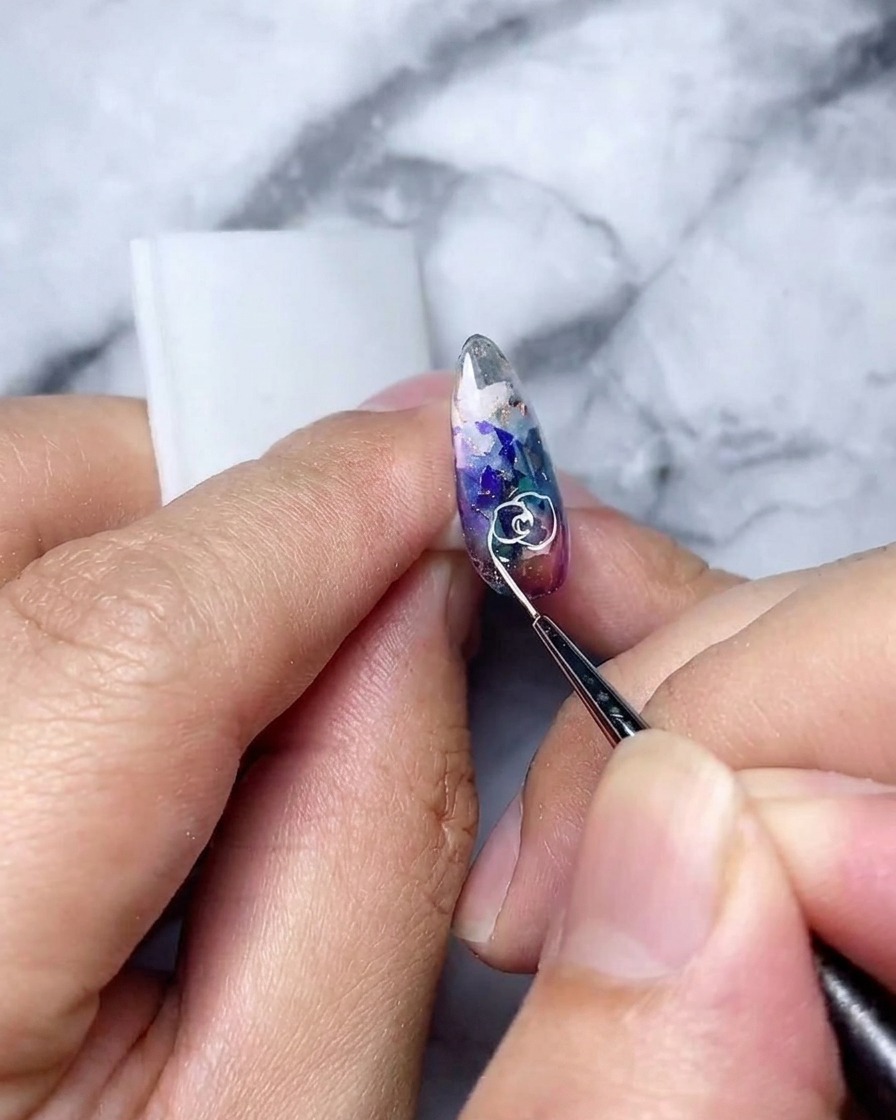 ホログラフィックなネイルの上に描かれた、完成した白い中抜きのバラの輪郭の詳細なショット。