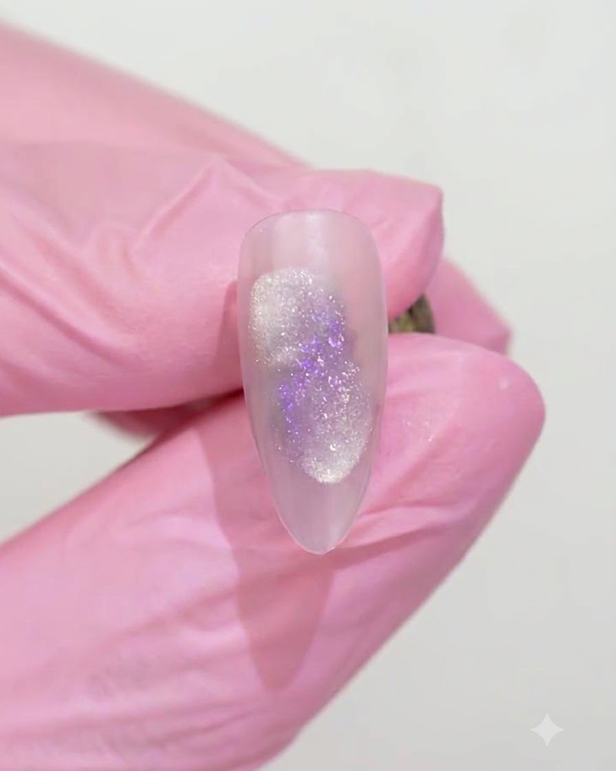 ピンクの手袋を着用した手が、UV/LEDランプの下で硬化されたマット仕上げのアーモンドシェイプネイルを持っている様子。