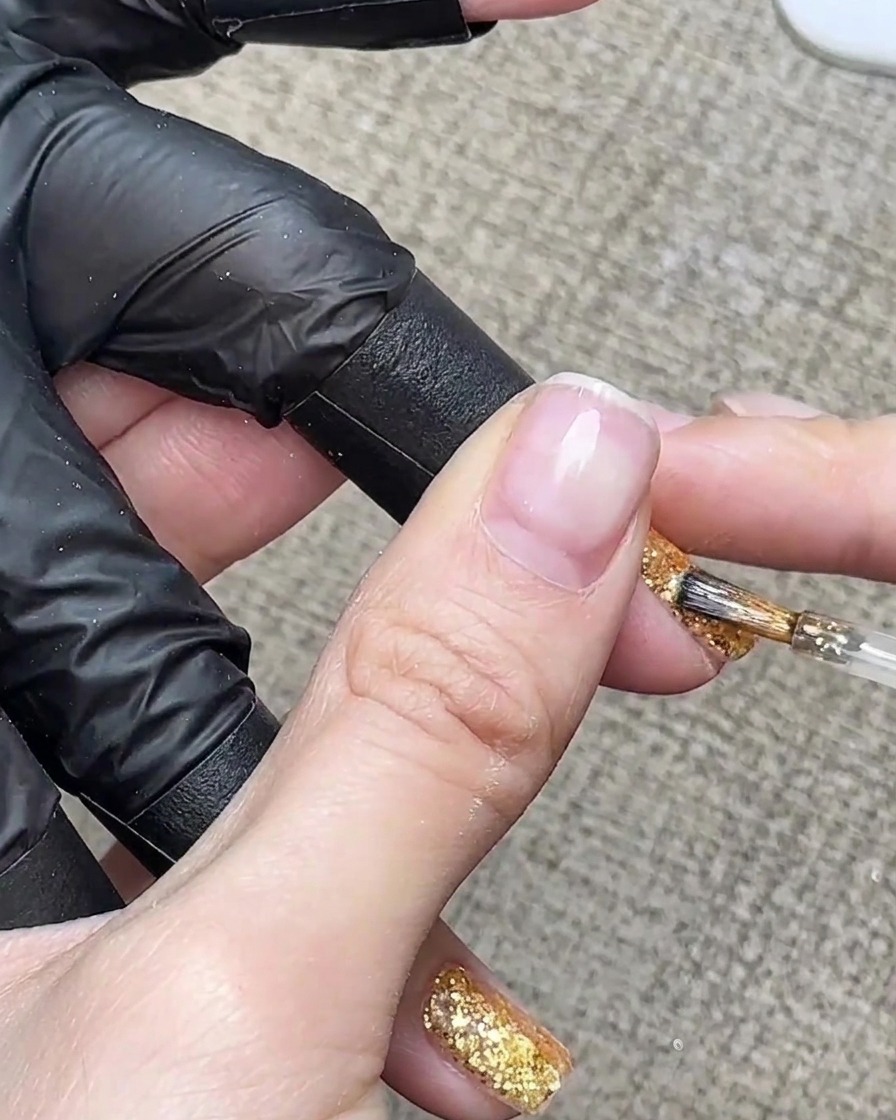 ゴールドグリッターネイルの先端に透明感のあるアンバーブラウンのジェルを詳細なブラシストロークで塗布している様子。
