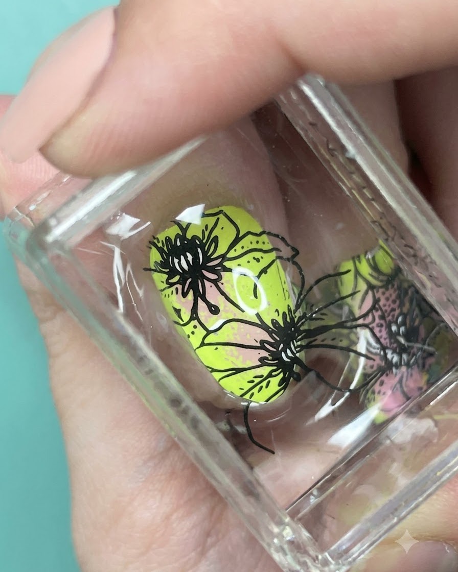 ネオンイエローとピンクのグラデーションネイルの上に配置された黒の花柄のクローズアップ。