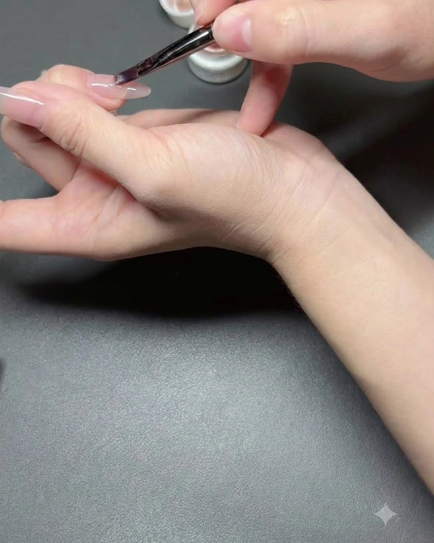 ネイルブラシを使って、爪に薄いヌード色のセミシアーポリッシュを塗布している様子。