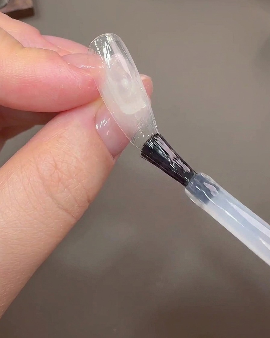 ネイルブラシを使ってクリアなネイルチップの境界線部分にビルダージェルを塗布している様子。