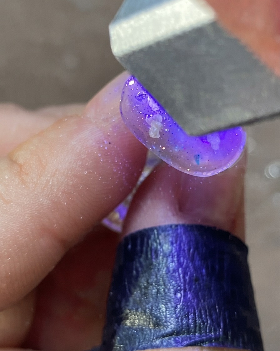 紫色のUV/LEDネイルランプの下で、デコレーションされたネイルデザインを硬化させている手。