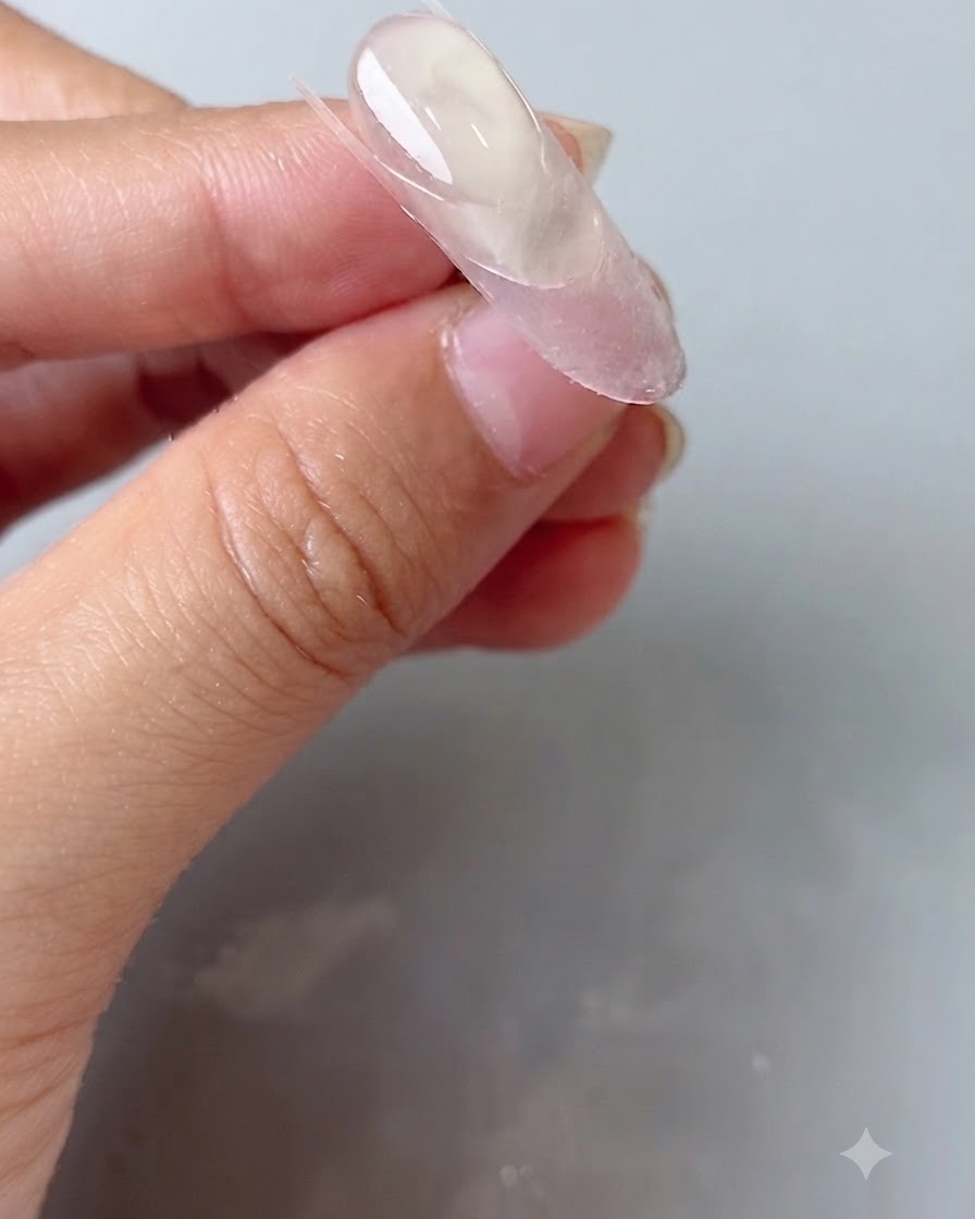 楕円形の爪の上にシリコンネイルツールでクリアなガイドシールを押し付けている様子。