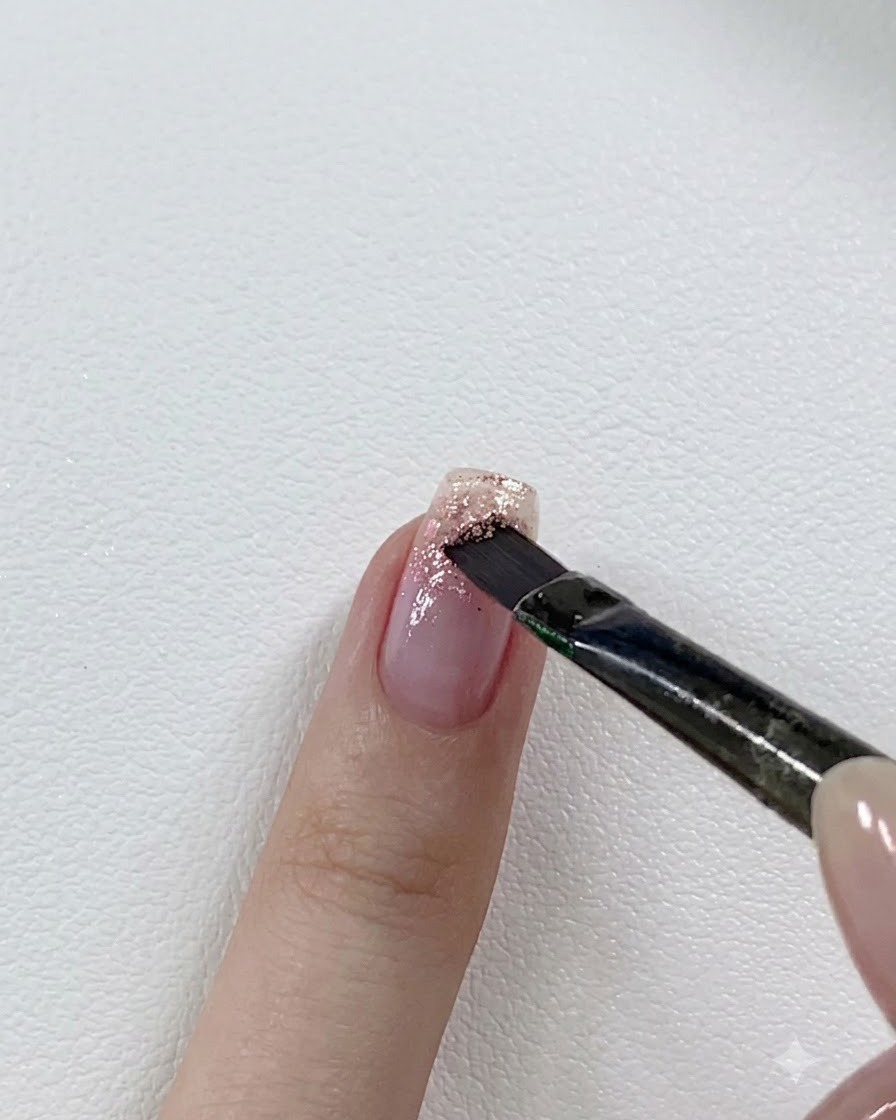 ネイルブラシが、部分的にグリッターを施した爪の先端に少し濃いピンクのグリッタージェルを重ねている様子。