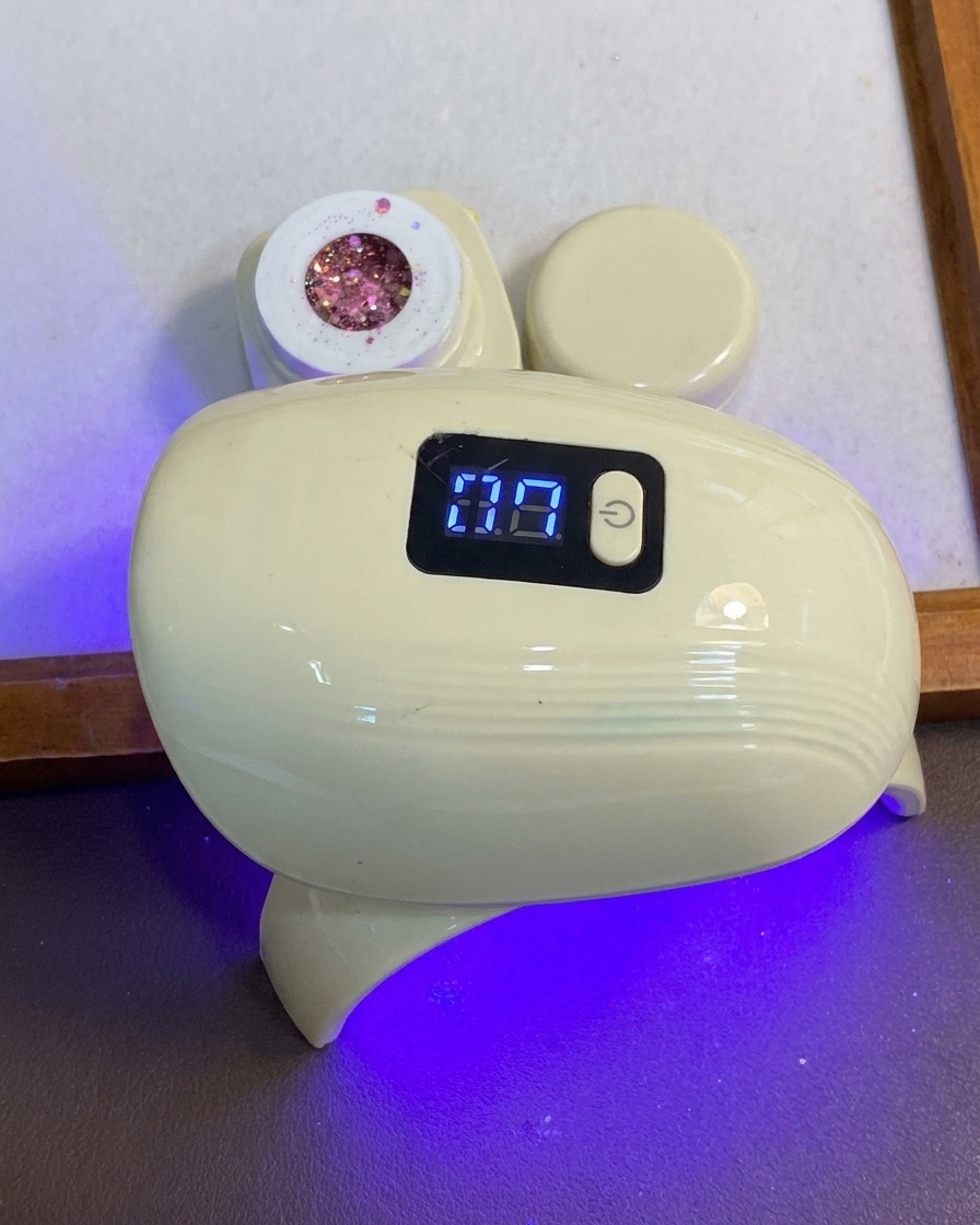 青と白のコンパクトなLEDネイル硬化ランプの下に手を置いて指をセットしている様子。